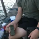 Customer photo of a man seated on a timber jetty with the MoskiCell unit resting on his leg