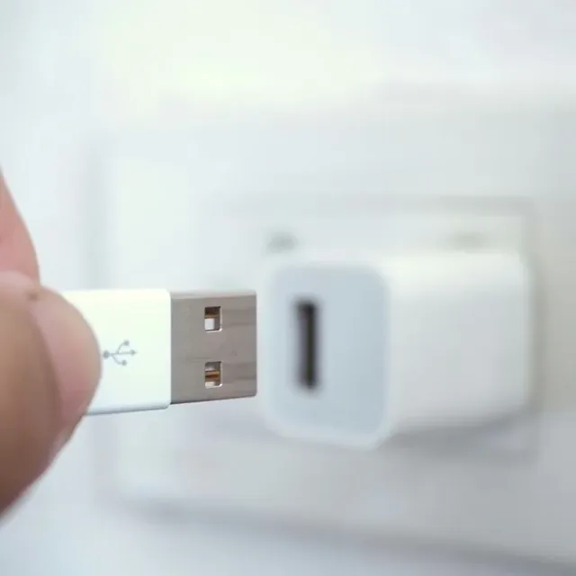 A hand plugging a white USB charging lead into a wall charger